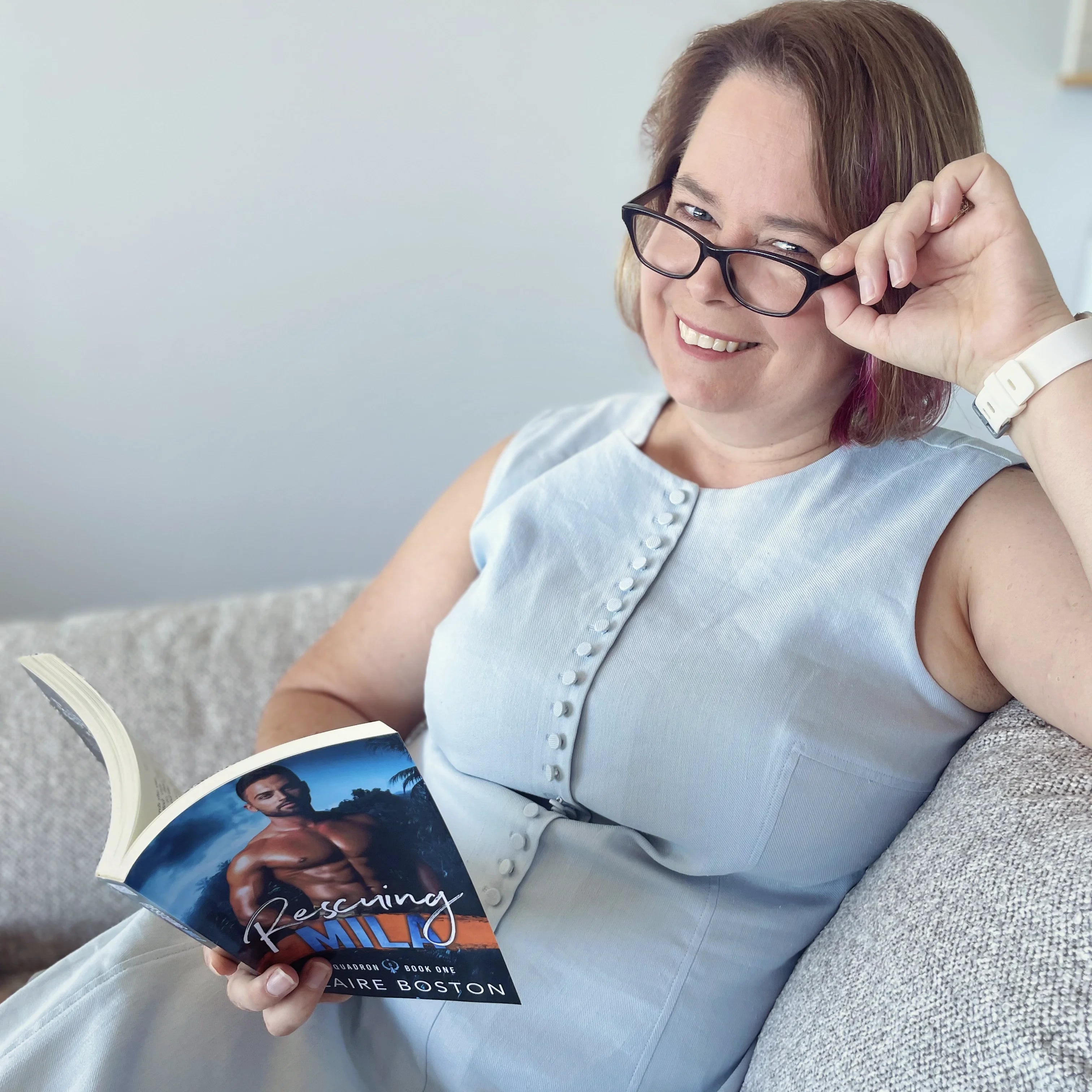 Claire Boston holding a book titled 'Rescuing Mila', sitting on a couch.