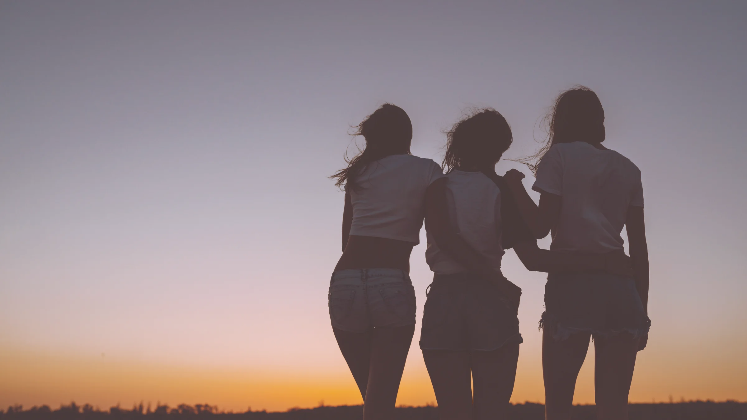 Three women standing together against a sunset sky