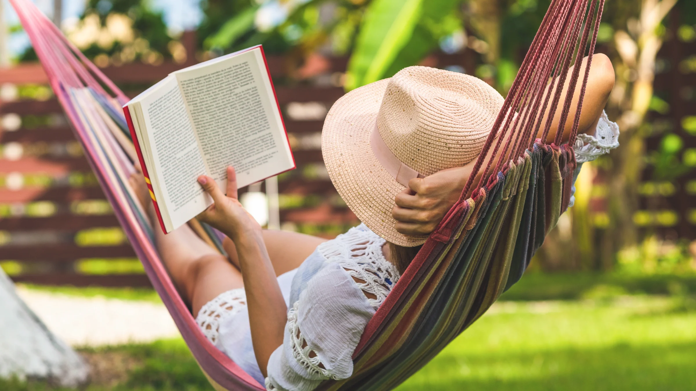 Person reading a book in a hammock with a straw hat on a sunny day.